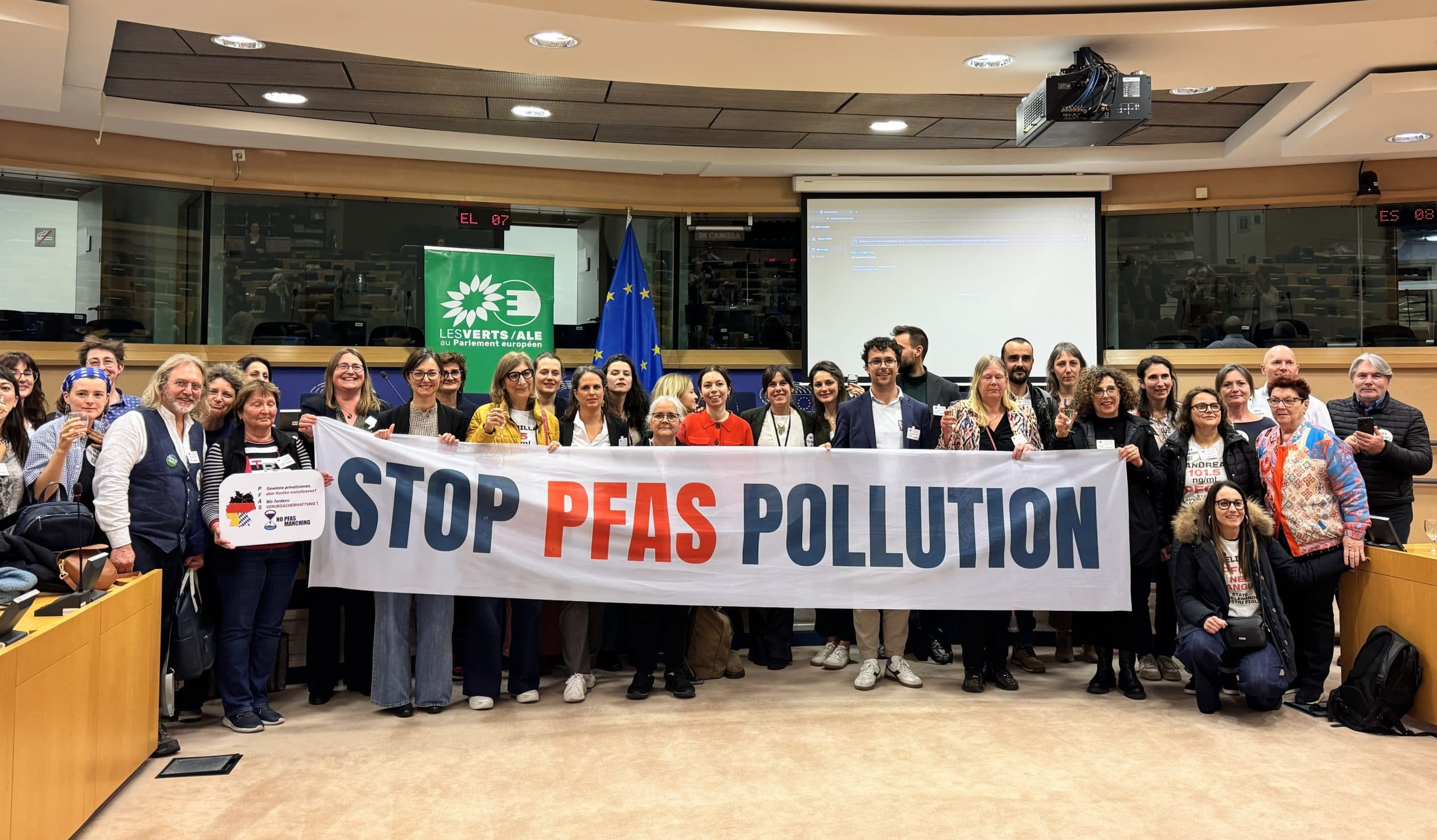A large group holding a “Stop PFAS pollution” banner in a European Parliament meeting room